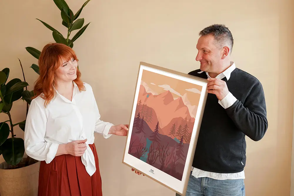 Un homme offre à sa femme l'affiche encadrée "Paysages de montagne avec ours bleu vert", illustration Yblou Création.